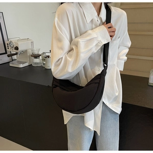 Model wearing a black crescent nylon crossbody bag with adjustable wide strap in a cafe