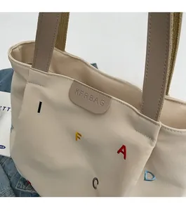 Detailed embroidery of colorful letters and premium leather logo tag on beige canvas tote
