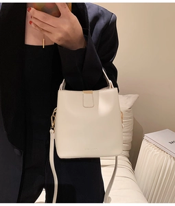 Detail of cream bucket bag showing gold hardware and embossed logo on soft vegan leather