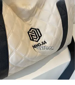 Detail der weißen gesteppten Handtasche mit schwarzem Logo und gewebtem Schultergurt