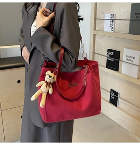 Detail of red canvas tote bag featuring metal chain strap and beige knit bear charm accessory