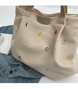 Close-up of colorful letter embroidery and leather logo on cream canvas tote bag