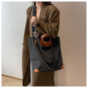 Bolso tote grande de lona negra con asas de cuero marrón llevado por una modelo elegante