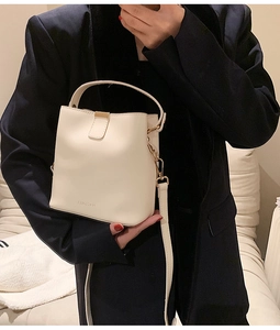 Detail of cream bucket bag with gold clasp and top handle shown on a black blazer