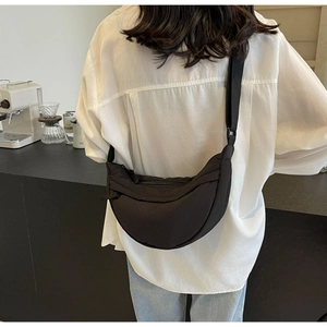 Minimalist black crescent crossbody bag shown in a lifestyle cafe setting