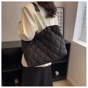 Model wearing a black quilted tote bag with gold chain strap in a modern room