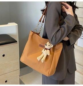 Brown canvas tote bag with chain strap and bear charm shown on model's shoulder