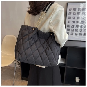 Detailed back view of a black quilted nylon tote bag with gold chain strap on model