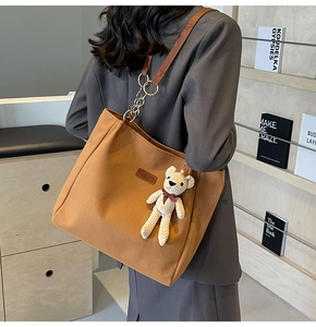 Detail of canvas tote bag with brown leather handles and cute knit bear charm