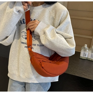Caramel orange crescent nylon crossbody bag worn by a model in a casual outfit