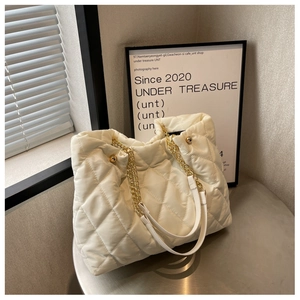 Detail of white quilted nylon tote bag with golden chain handle and soft bubble texture
