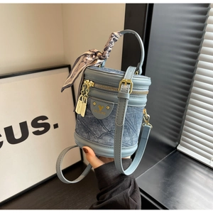 Détail du sac seau en denim et cuir avec finitions dorées et foulard en soie à motif