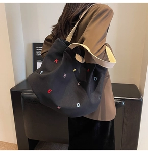 Detail of black canvas tote bag featuring multicolor letter embroidery and leather logo