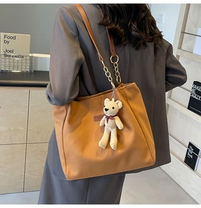 Detail of warm brown canvas tote bag featuring leather metal chain strap and bear charm