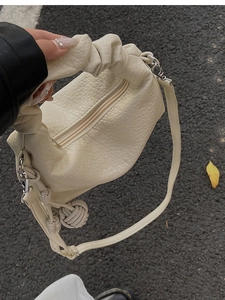 Gros plan du sac à main plissé crème avec cuir grainé et breloque en forme de boule