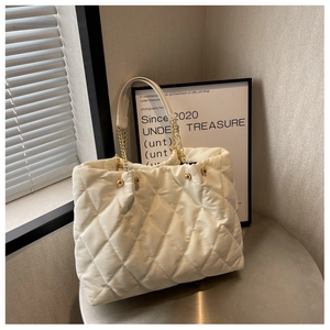 Close-up of beige quilted tote bag featuring golden chain straps and bead hardware