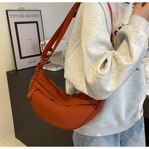 Detail of dark orange nylon crossbody bag with zipper and long fabric strap