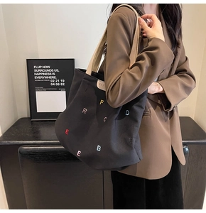 Close-up of colorful letter embroidery and faux leather detail on black canvas tote bag
