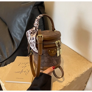 Détail d'un sac seau cylindrique marron avec foulard en soie sur un socle en pierre