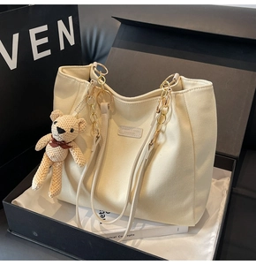 Detailed view of beige canvas tote bag with gold chain strap and teddy bear charm in a gift box
