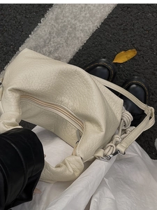Détail d'un sac à bandoulière en cuir grainé beige avec poignée nouée plissée et zip argenté