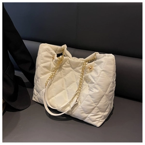 Close-up of quilted nylon tote bag featuring gold chain strap and metallic ball detail