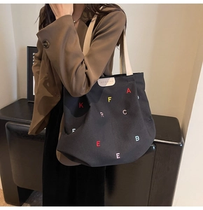 Detail of black canvas tote bag with colorful letter embroidery and white strap