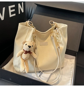 Detail of beige canvas tote bag with gold chain handles and cute bear charm accessory