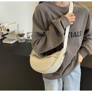 Beige nylon crescent crossbody bag styled on a model in a casual cafe setting