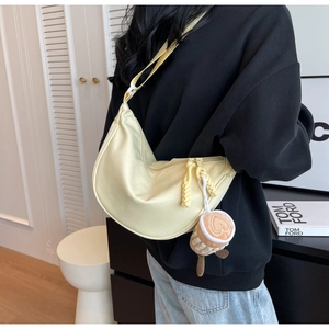 Close-up of pale yellow nylon half-moon crossbody bag with cute plush charm on strap