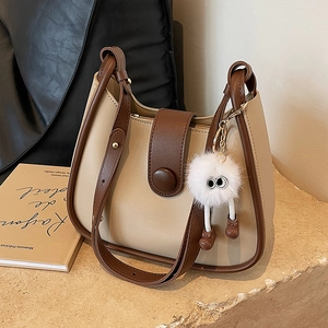 Minimalist beige and brown bucket bag with plush charm on a stone display stand