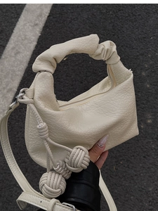Détail du sac à bandoulière plissé crème avec pendentifs décoratifs en boules tressées