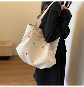 Detail of off-white canvas tote bag with colorful letter embroidery and branding tag