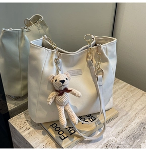 Detail of off-white canvas tote with golden chain strap and cute knitted bear charm