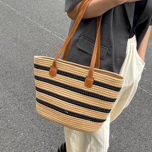 Large beige woven straw tote bag with black stripes and brown leather handles