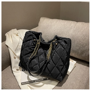 Macro detail of black quilted nylon tote bag with golden metal chain strap on sofa