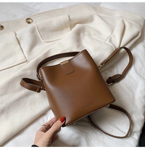 Detail of brown leather bucket bag with embossed logo and metal buckle on soft fabric