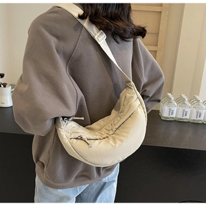 Rear view of a light beige nylon crescent bag with adjustable wide strap on a model