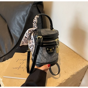 Détail d'un sac seau cylindrique en denim avec garniture cuir et foulard sur pierre