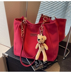 Detail of burgundy tote bag with gold chain strap, luxury fabric, and cute bear charm