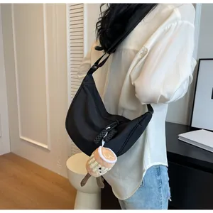 Black crescent nylon bag shown in use with a latte plush charm on the shoulder strap