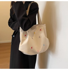 Close-up of cream canvas tote bag with colorful embroidery and branded leather tag