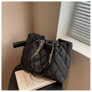 Close-up of black quilted nylon tote bag with golden chain straps and rivet details