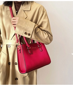 Detail of red bridal leather handbag with gold logo worn by a model in a trench coat