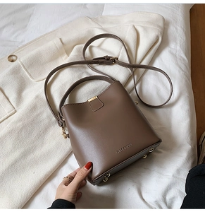 Detail of a brown leather bucket bag with gold metal clasp and brand logo on fabric