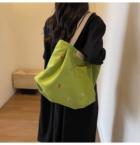 Detail of green canvas tote bag with colorful letter embroidery and branding tag