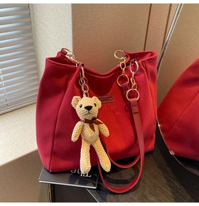 Close-up of red canvas tote bag featuring golden chain strap and knit bear charm