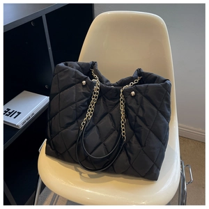 Close-up of black quilted nylon tote bag with golden chain strap on a white chair