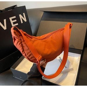 Detail of a minimalist orange nylon crescent shoulder bag with adjustable strap