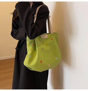 Detail of vibrant green canvas tote bag with colorful letter embroidery and leather tag